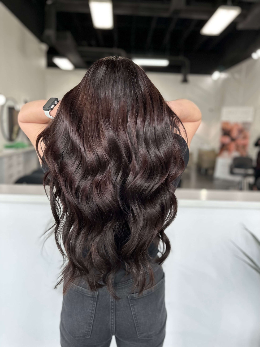 Person showcasing long, wavy dark hair in a salon setting, highlighting fresh hair transformation.