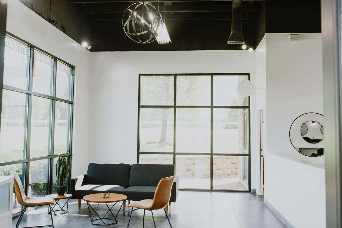 Modern interior of a hair salon with black sofa, wooden coffee table, and large windows allowing natural light.